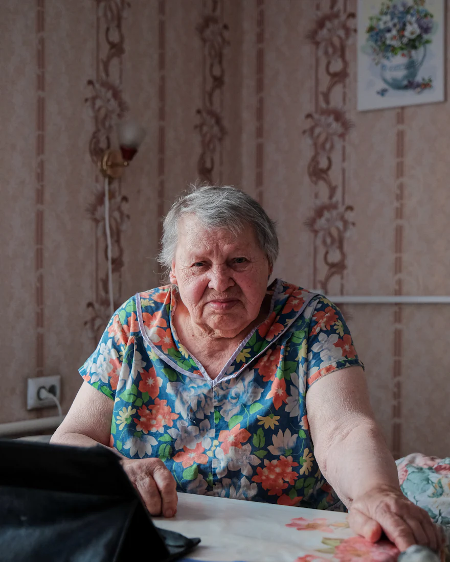 Oudere vrouw aan een tafel kijkt rustig in de camera